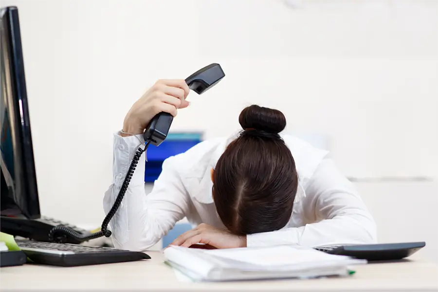 woman with her head on her desk dealing with phone system frustrations